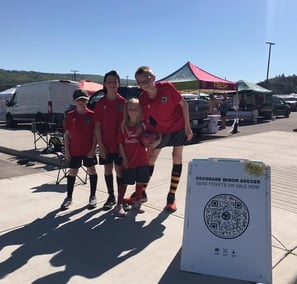 Four youth behind a sandwich board sign with a QR code to promote raffle tickets