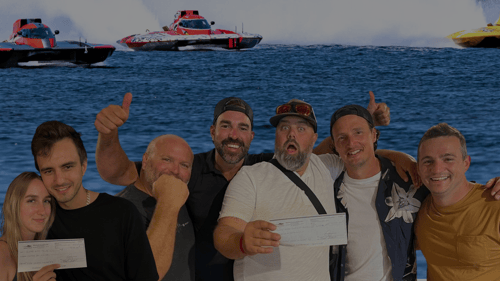 Line of people holding up their winning cheques in front of a water and boat background